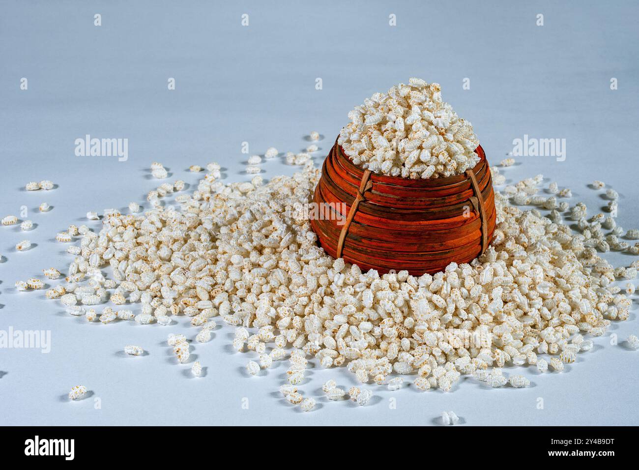 Indian traditional handcrafted cane pot named by Kunke Overflowing with Scattered Popped Rice or Khoi on White Background, food photography Stock Photo