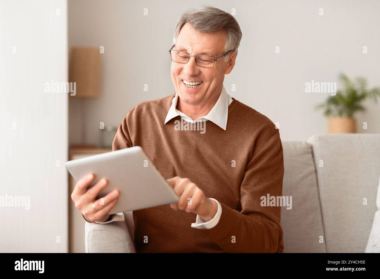 Senior Man With Tablet Computer Browsing Internet Sitting On Sofa Stock Photo