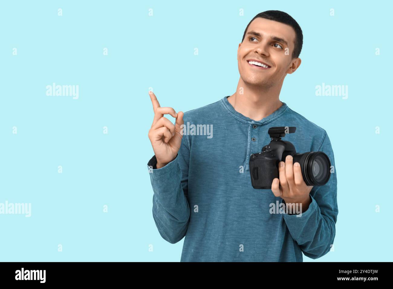 Male photographer with modern camera pointing at something on blue background Stock Photo