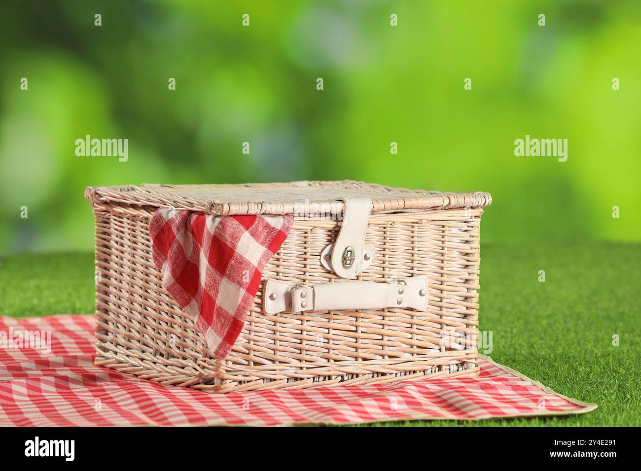 One picnic wicker basket with checkered napkin and blanket on grass ...