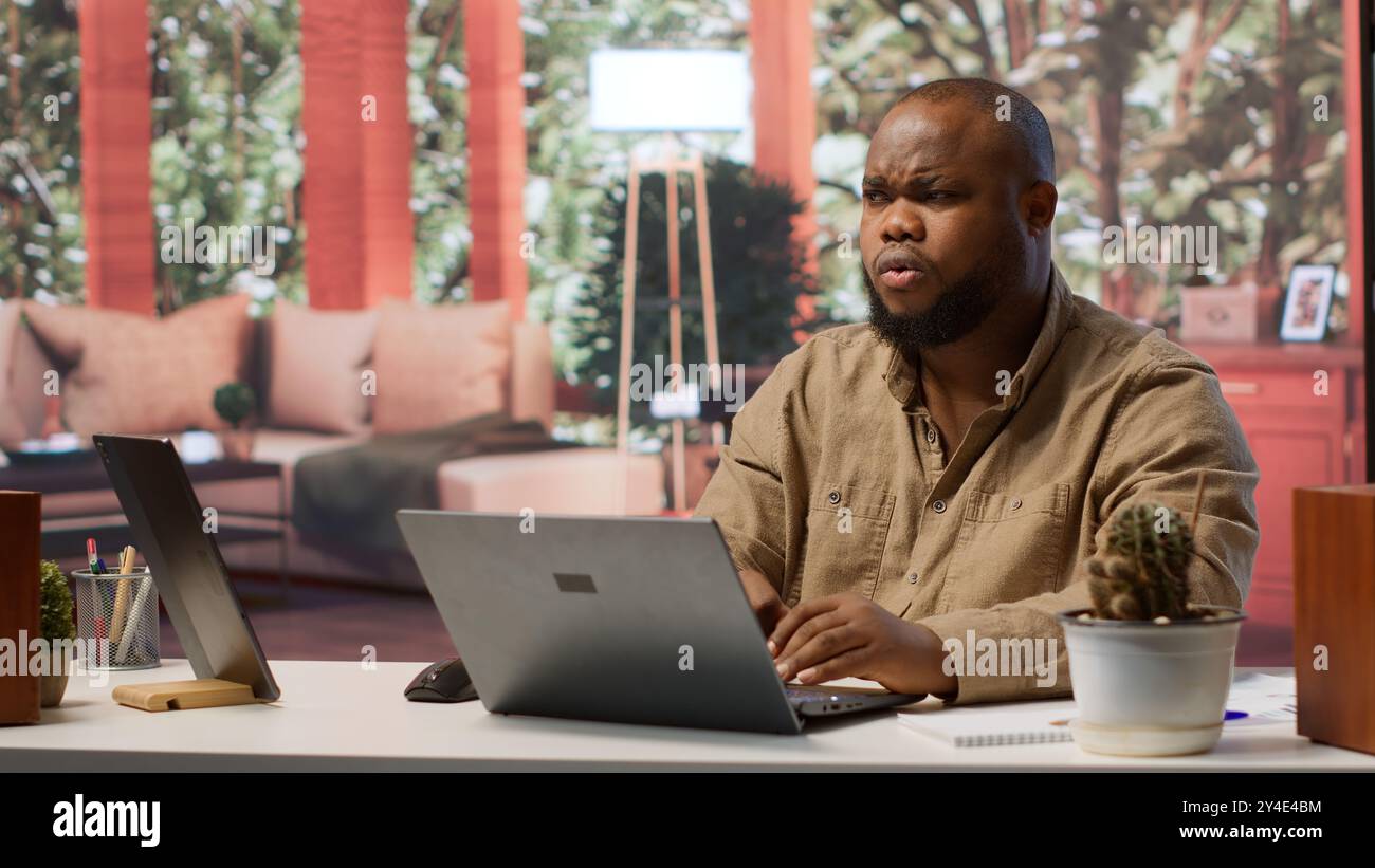 Freelancer managing startup projects and thinking about client needs from his home office, developing new growth strategy. Self employed analyst does telecommuting work on laptop. Camera A. Stock Photo