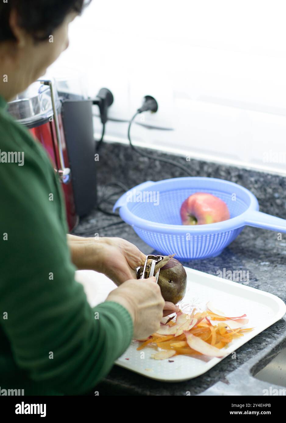 Elderly woman meticulously peels beetroot for a nutritious juice blend Stock Photo