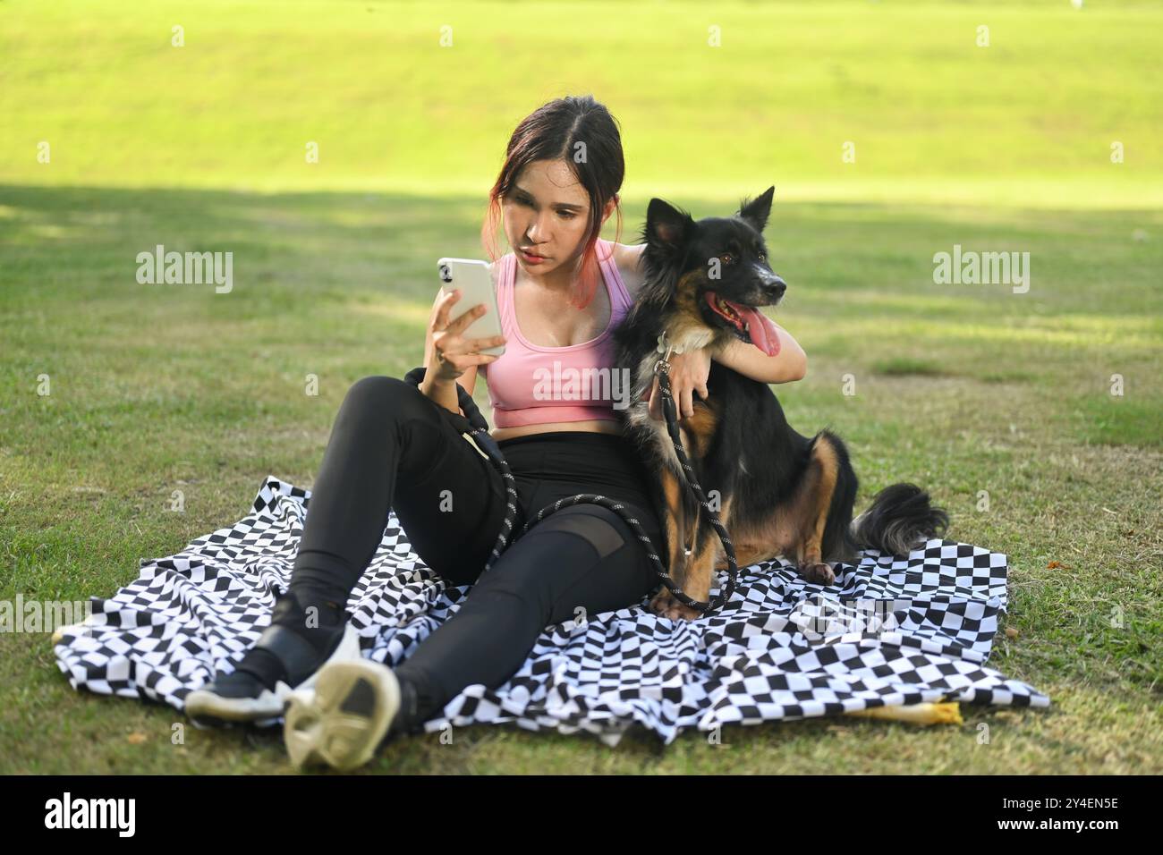 Happy young woman sitting on a blanket in a park and taking a selfie ...