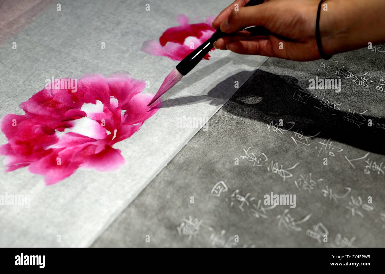 (240918) -- BEIJING, Sept. 18, 2024 (Xinhua) -- Qian Xiayu paints peonies on a rubbing work at the Luoyang Huaxia Rubbing Culture Museum in Luoyang City, central China's Henan Province, Sept. 11, 2024. Jinshi Bogu, an intangible cultural heritage of Luoyang, refers to the painting created on the paper already marked with inked characters and patterns that are made with rubbing techniques. The combination of the characters and patterns, initially engraved on stones or ancient artifacts, with the hand painting images and calligraphy by an artist, represents the integration of the different Stock Photo