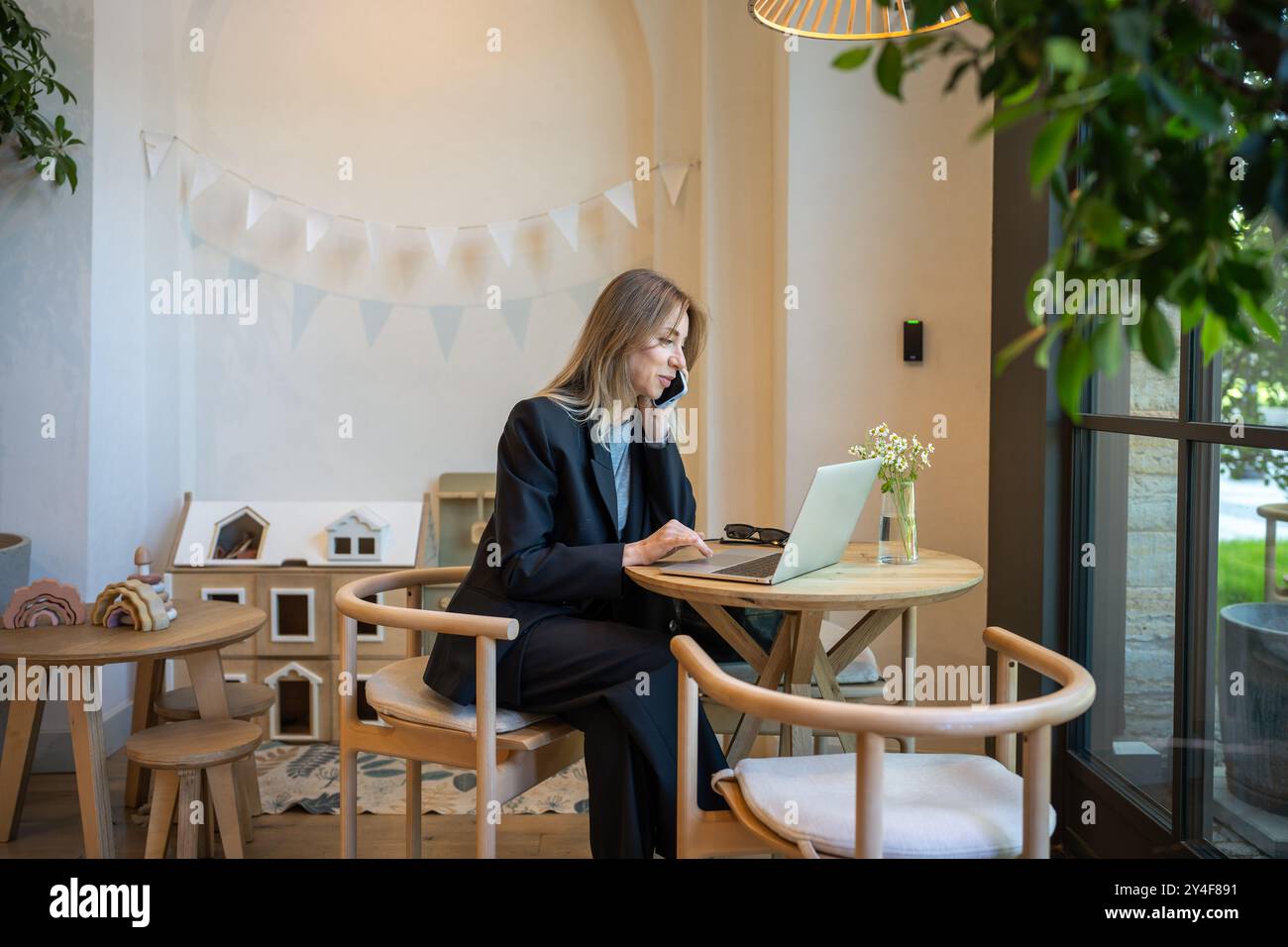 Thoughtful woman in business suit calling on phone sits with laptop in cafe pensive looks to window Stock Photo