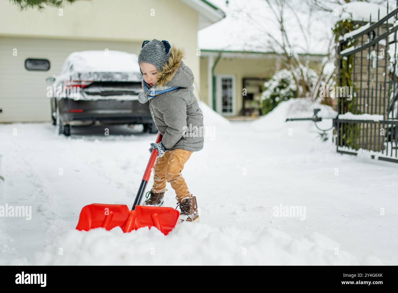 Adorable little boy helping to shovel snow in a backyard on winter day. Cute child wearing warm clothes playing in a snow. Winter activities for famil Stock Photo