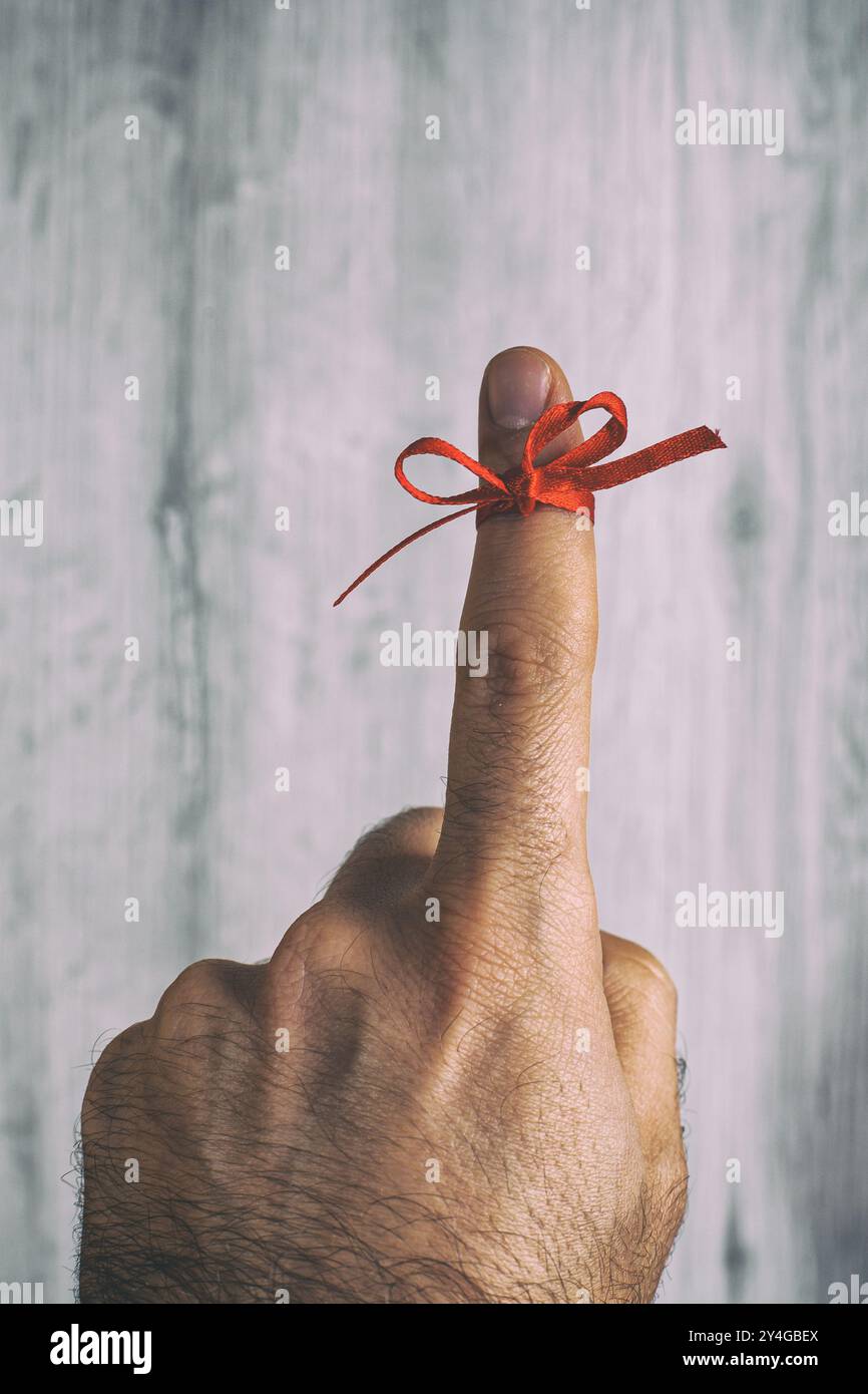 Man is showing his finger with a red ribbon tied around it, serving as ...
