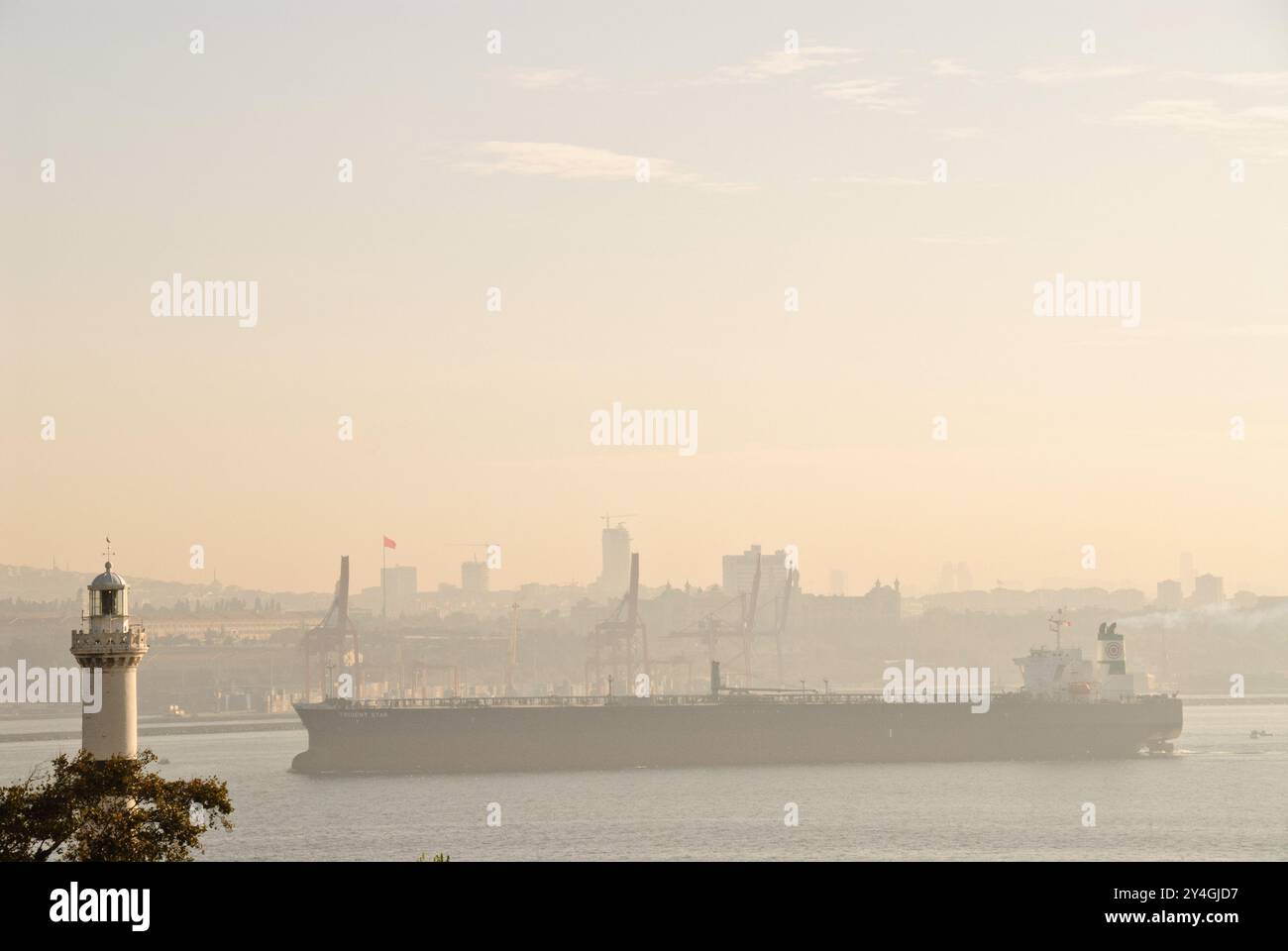 Cargo Ship Bosphorus Strait Istanbul Turkey // ISTANBUL, Turkey — A large cargo ship navigates the strategic intersection where the Sea of Marmara, the Golden Horn, and the Bosphorus Strait converge in Istanbul, passing in close proximity to a lighthouse. The Bosphorus Strait serves as a crucial maritime corridor connecting the Black Sea to the Mediterranean, handling approximately 48,000 vessels annually transporting over 3 million barrels of oil per day. This narrow waterway, which divides Istanbul between Europe and Asia, represents one of the world's busiest and most strategically importan Stock Photo
