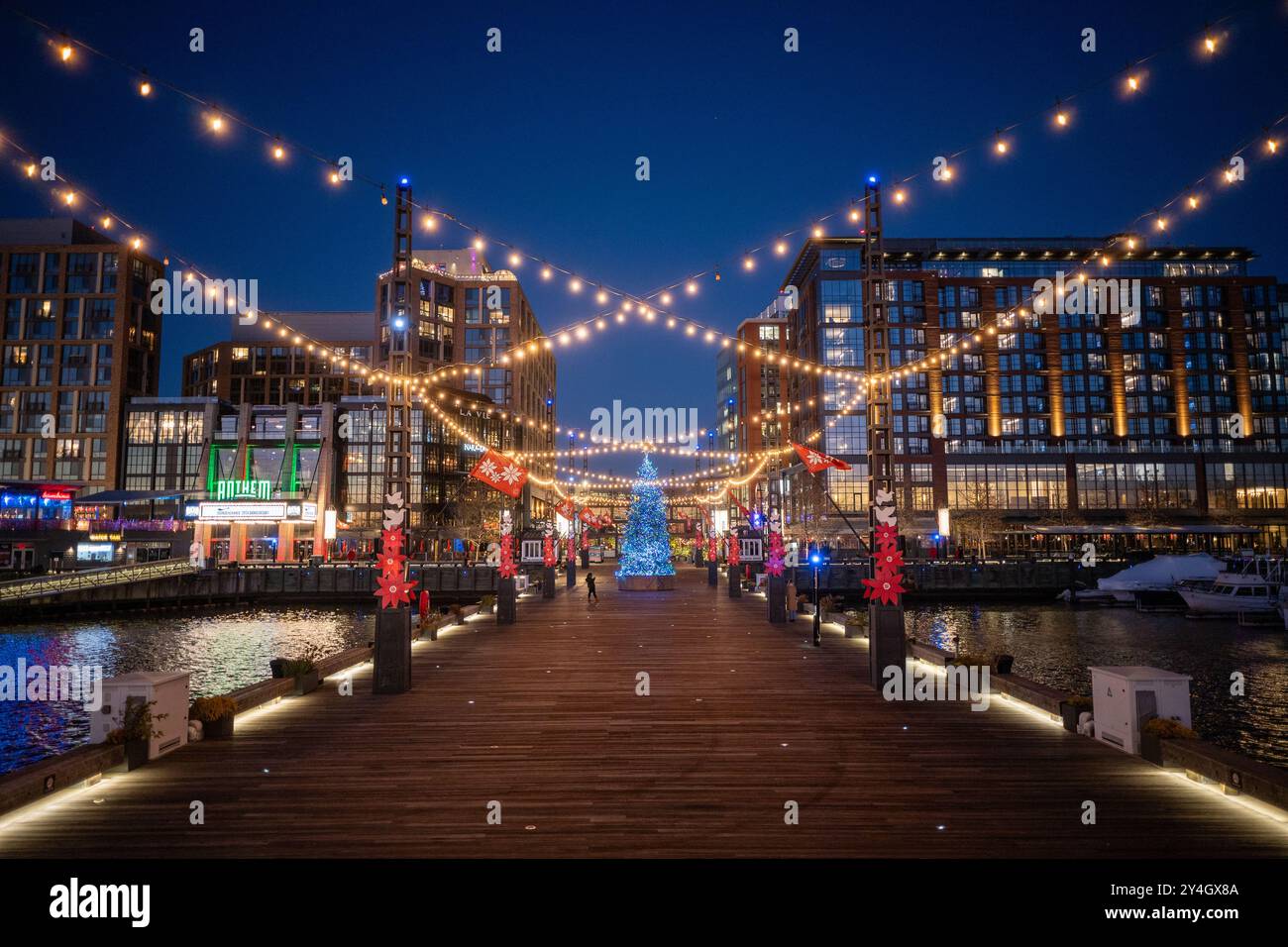 The Wharf Holiday Lights Washington DC // WASHINGTON DC — The Wharf, a vibrant waterfront neighborhood in Washington DC, is illuminated with festive holiday lights at night. The colorful display reflects off the Washington Channel, creating a magical winter scene along the Potomac River and showcasing the area's blend of modern development and seasonal charm. Stock Photo