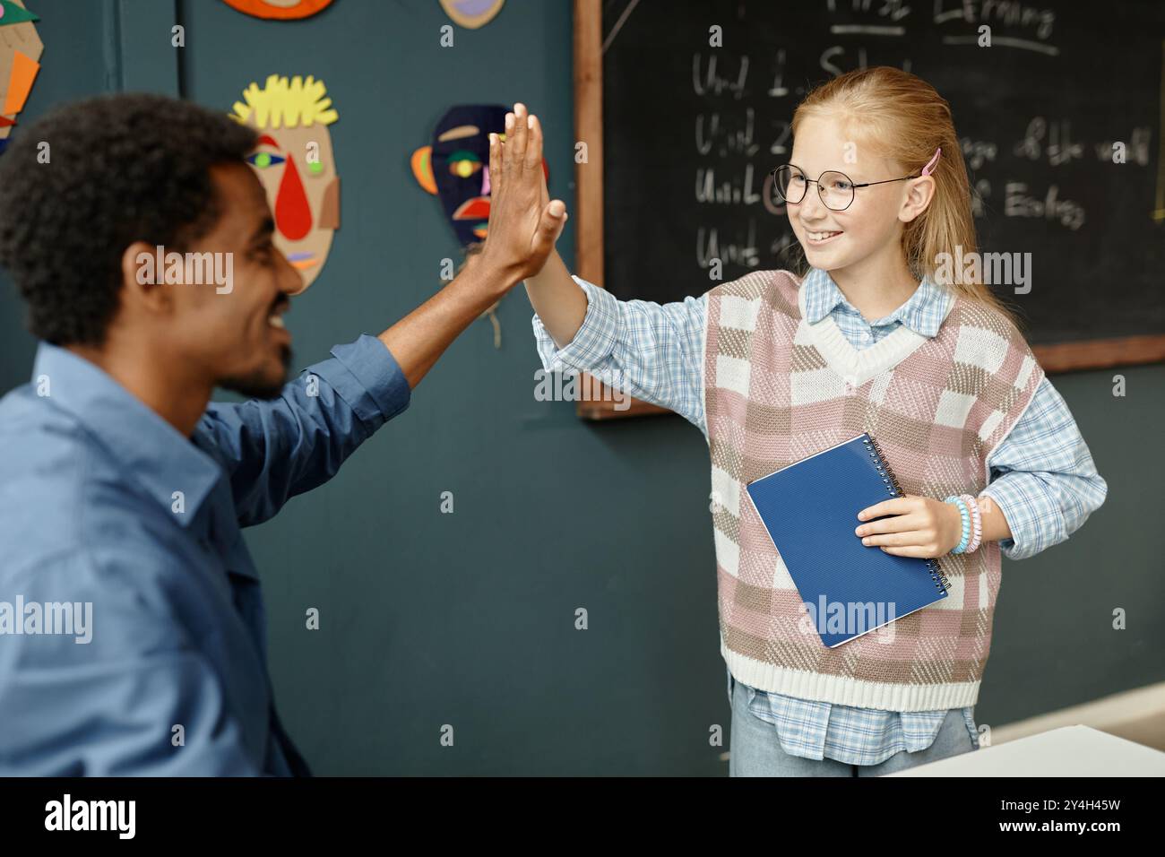 Medium shot of cheerful young female student high fiving male teacher while receiving praise for excellent job during lesson at primary school, copy s Stock Photo