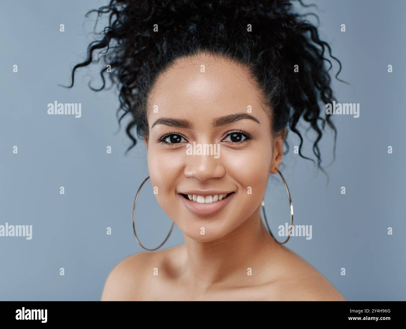 Portrait of a smiling female with curly hair and earrings looking at camera over blue backdrop Stock Photo