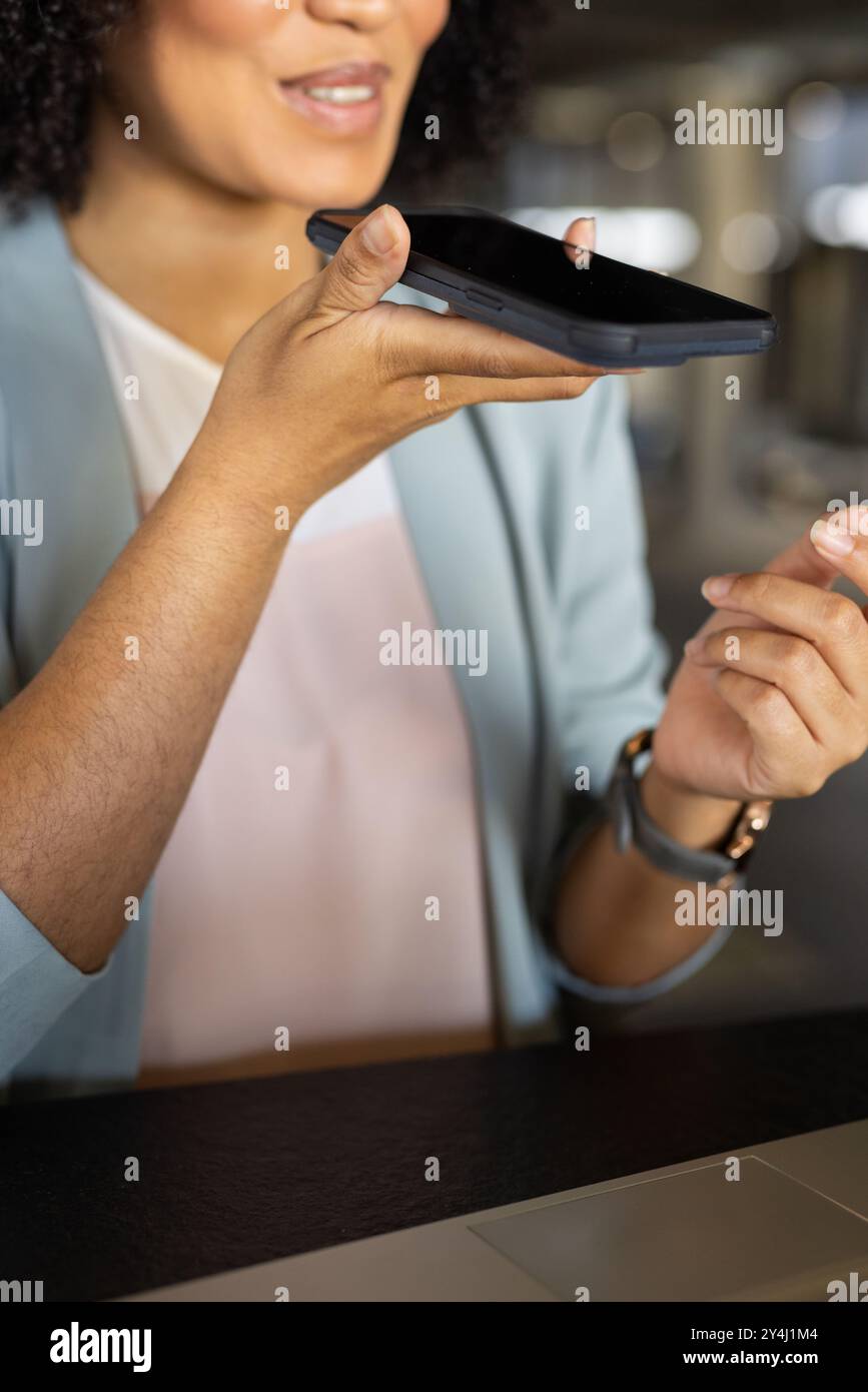 Holding smartphone, woman using voice command feature in modern office setting Stock Photo