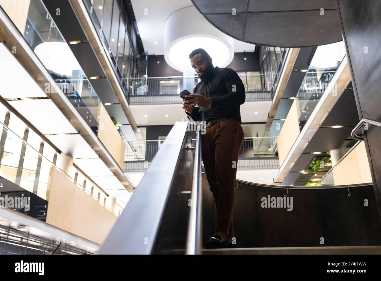 Businessman using smartphone while walking down stairs in modern office building, copy space Stock Photo