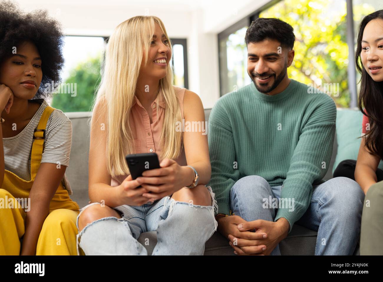 diverse friends sitting on couch, smiling and using smartphone, enjoying time together Stock Photo