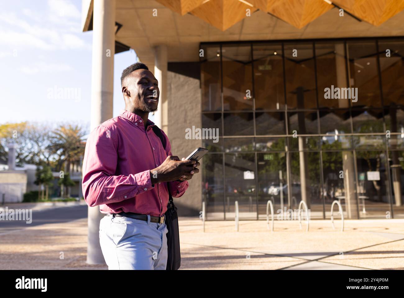 Walking outside modern office building, man holding smartphone and smiling, copy space Stock Photo