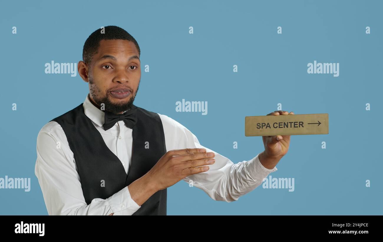 Hotel employee in tuxedo pointing people to the spa center using a wall ...