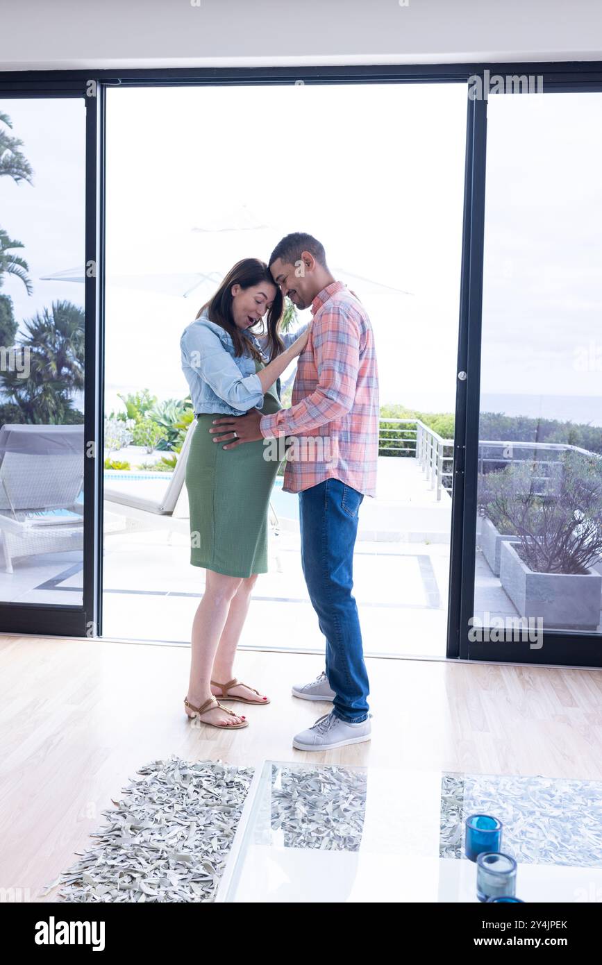 At home, expecting multiracial couple standing together Stock Photo