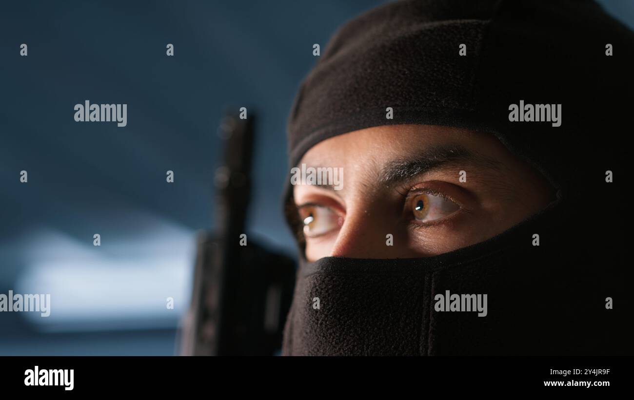Terrorist hiding identity, attacking enemy command center. Close up of masked insurgent inspecting room during enemy base assault hijacking in guerilla warfare armed conflict, camera A Stock Photo
