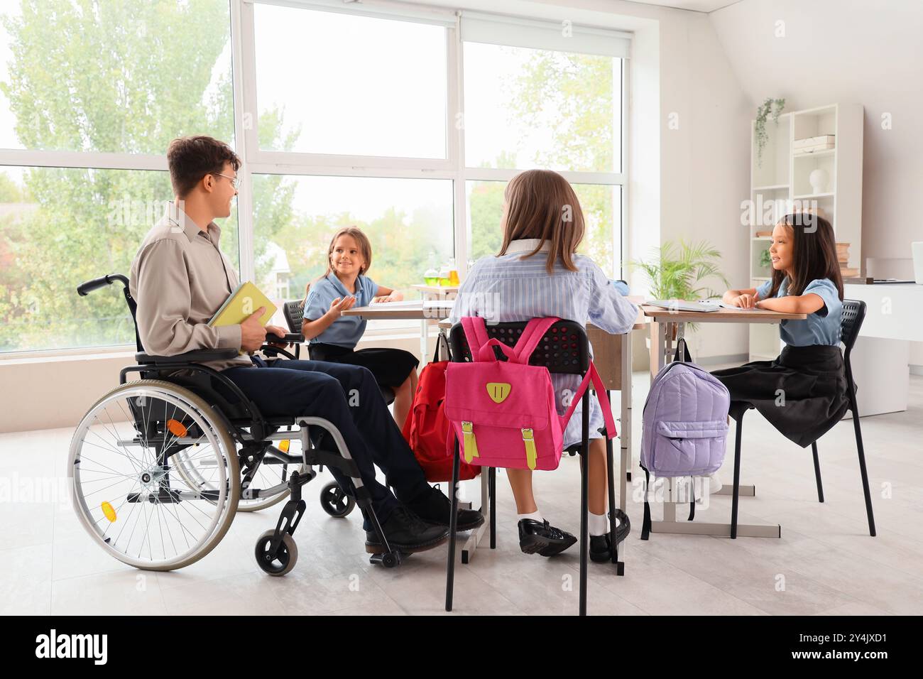 Male teacher in wheelchair conducting lesson to little pupils at school ...