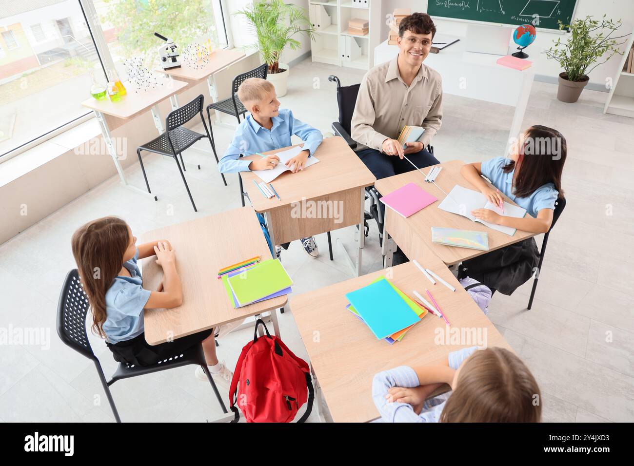 Male teacher in wheelchair conducting lesson to little pupils at school ...