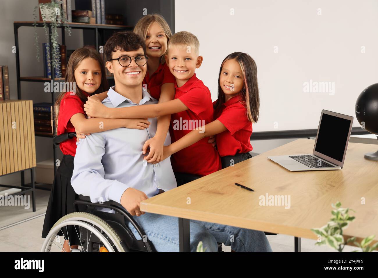 Male teacher in wheelchair with little pupils hugging at school Stock ...