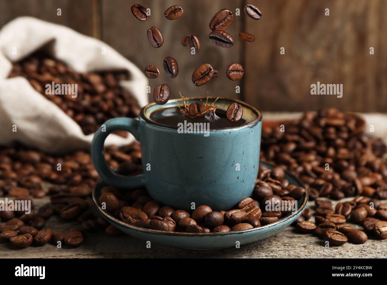 Roasted beans falling into cup with aromatic coffee on wooden table ...