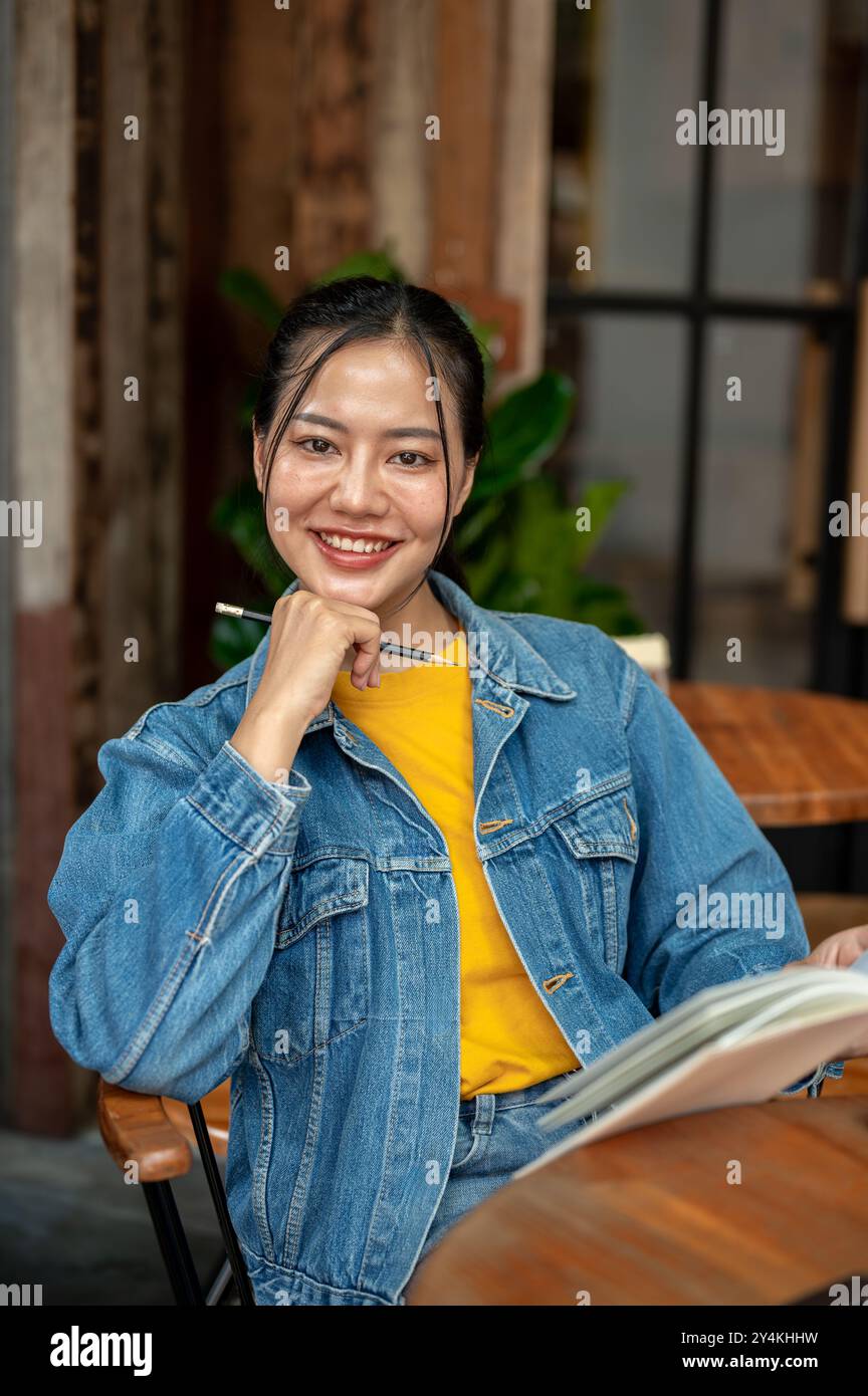 A charming, positive Asian woman in a denim jacket is reading a book ...