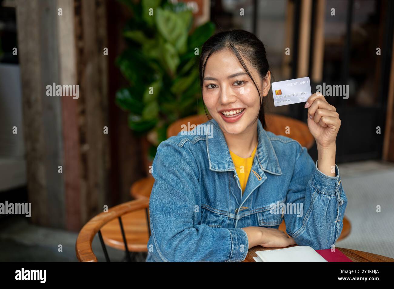 A charming, smiling Asian woman in a denim jacket is sitting in a ...
