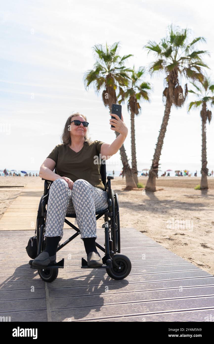 Mature woman in a wheelchair taking a selfie with her cell phone on the ...