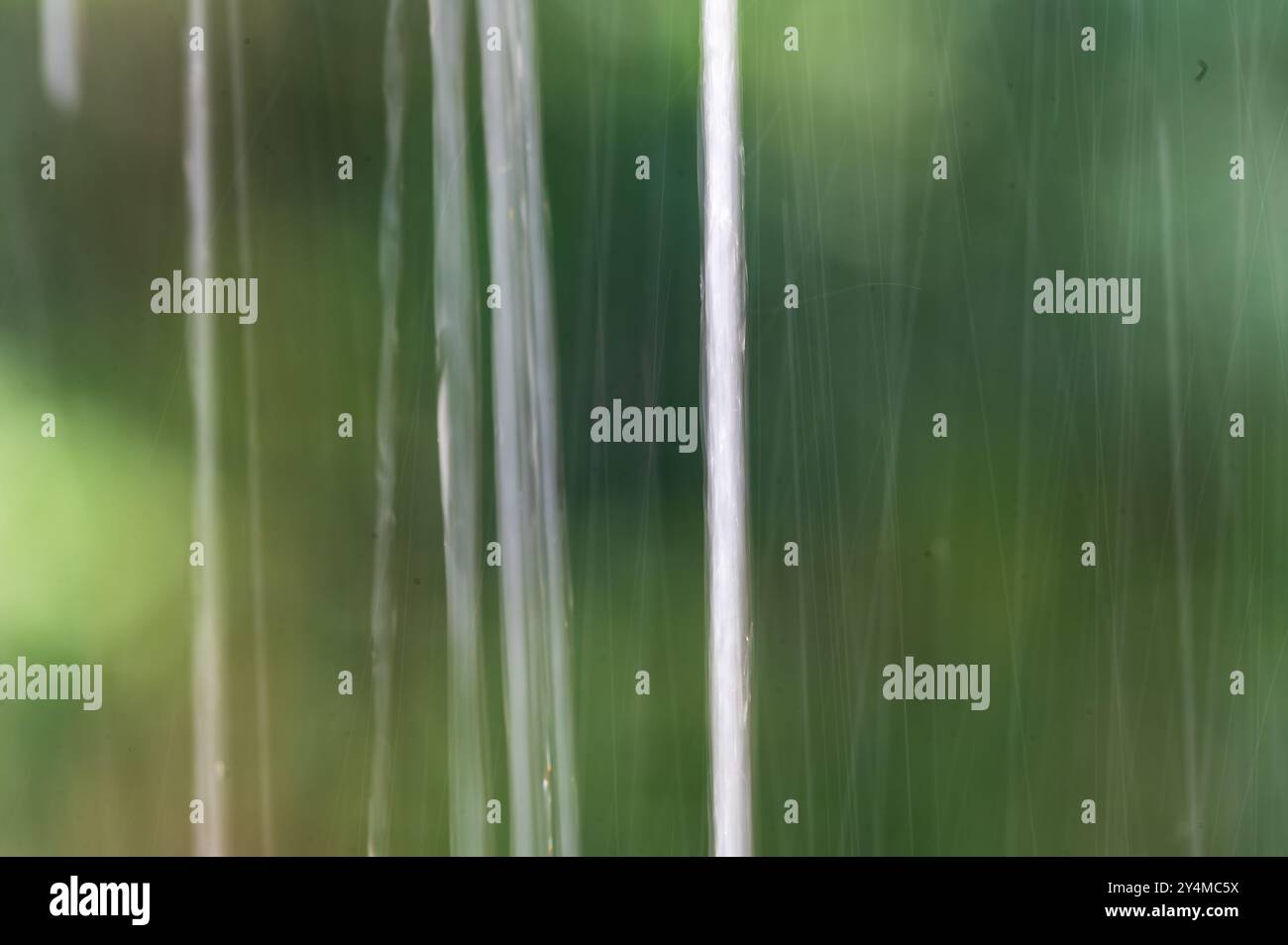 Close-up of raindrops streaming down a windowpane. The soft focus and blurred background create a serene and calming atmosphere. Stock Photo