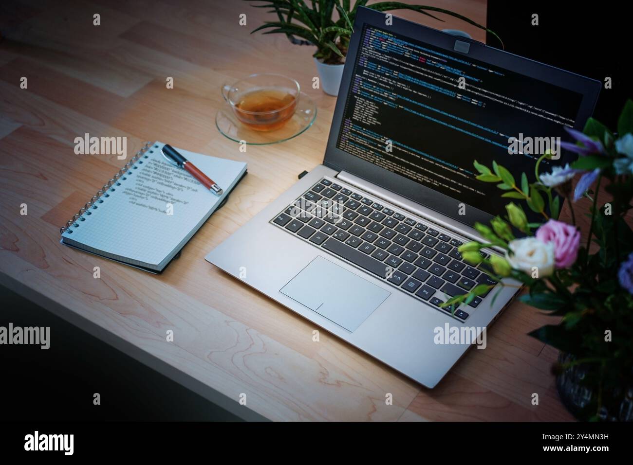 Laptop with code on the screen and notepad with handwritten code on a wooden desk at night, freelancer overtime in software development or virus defen Stock Photo