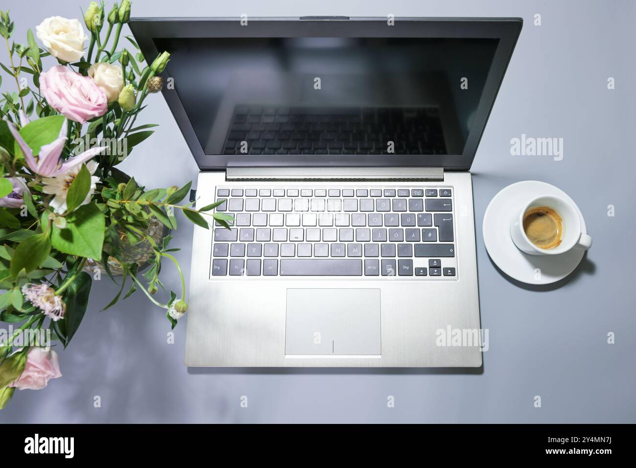 Silver colored laptop on a gray desk with a bouquet of flowers and a coffee cup, business workplace or home office, top view from above, copy space, s Stock Photo