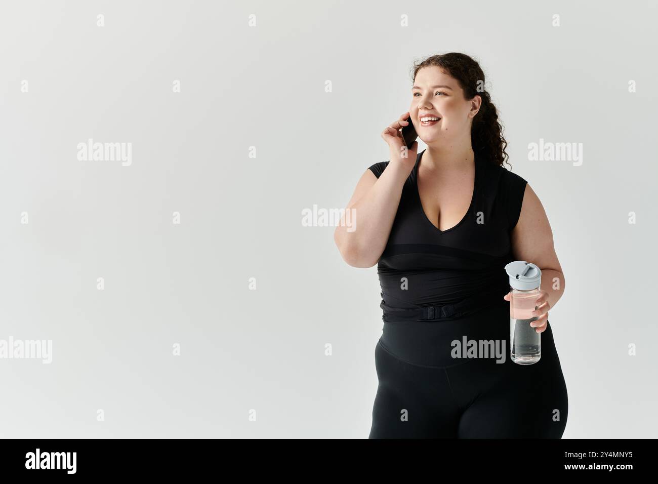 A stylish plus size woman smiles brightly, chatting on her phone while ...