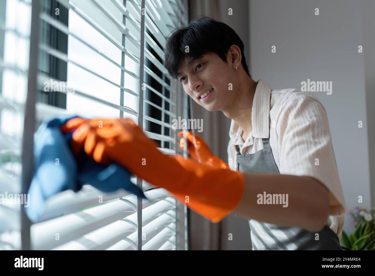 Young Man Cleaning Window Blinds with Orange Gloves and Blue Cloth in a ...