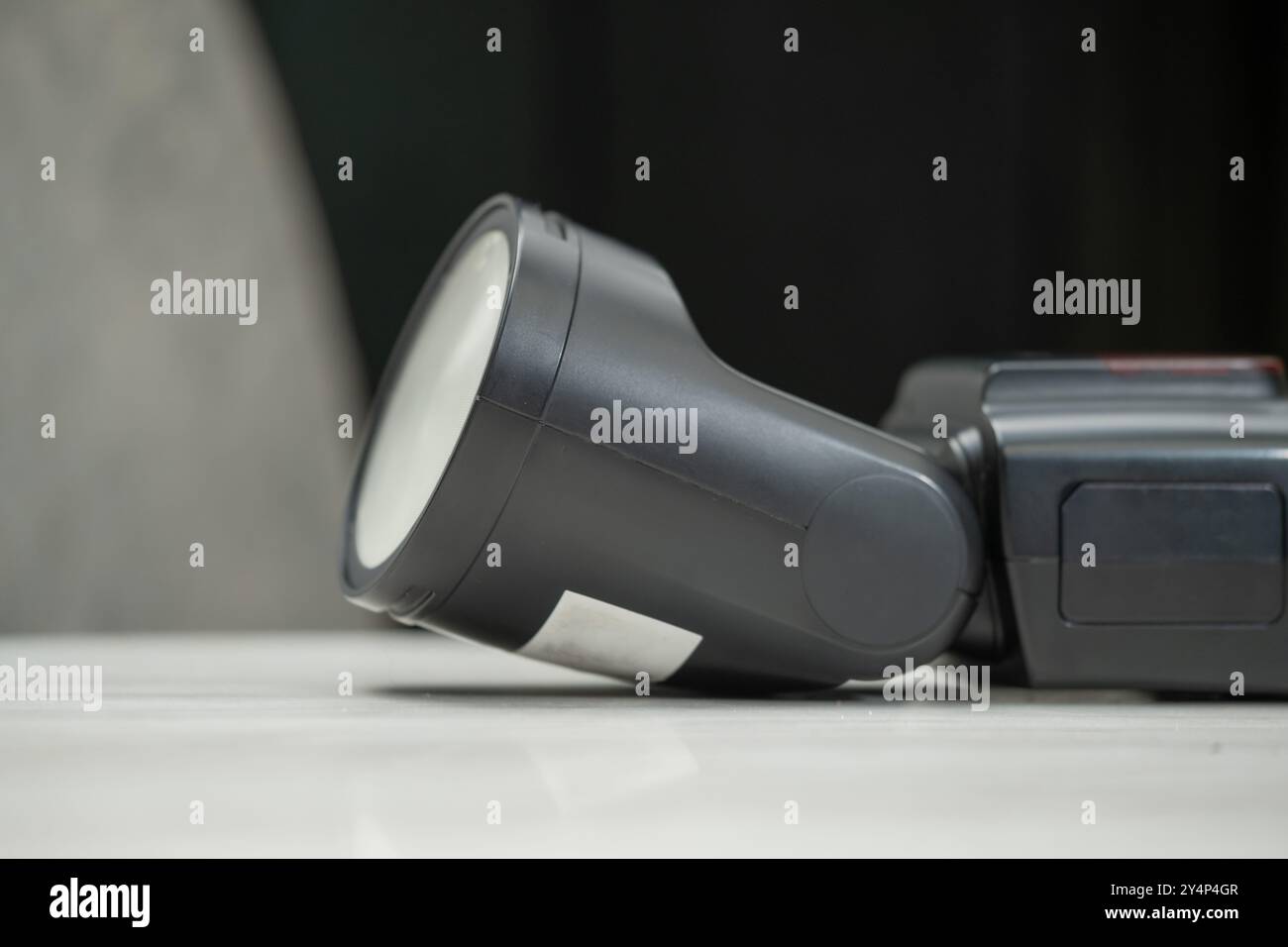 A close-up of a professional camera flash unit resting on a marble surface. The flash is black with a silver reflector, showcasing its design and func Stock Photo