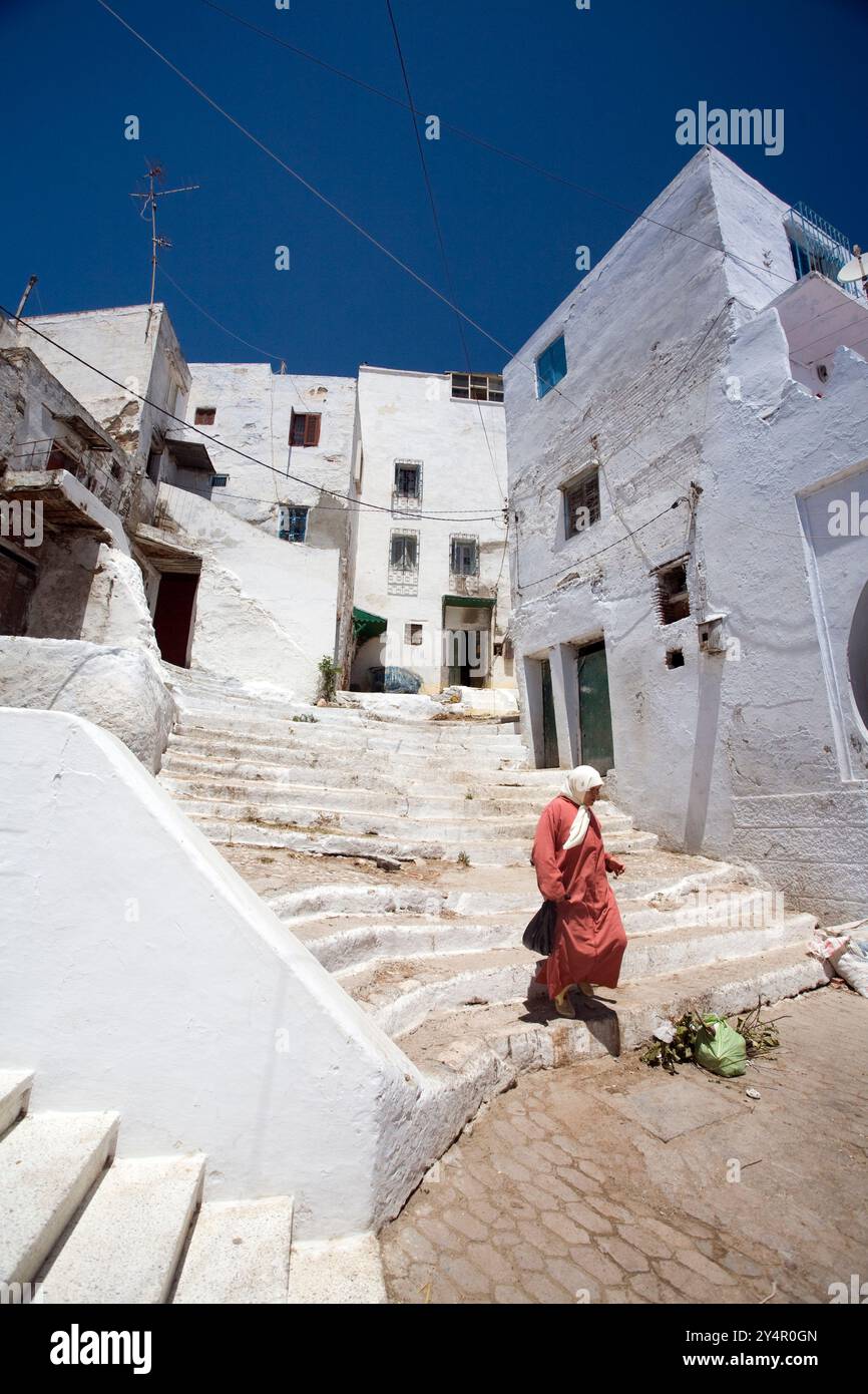 A woman walks down the steps of a charming whitewashed alley in Tetouans historic Medina, showcasing the vibrant local architecture. Stock Photo