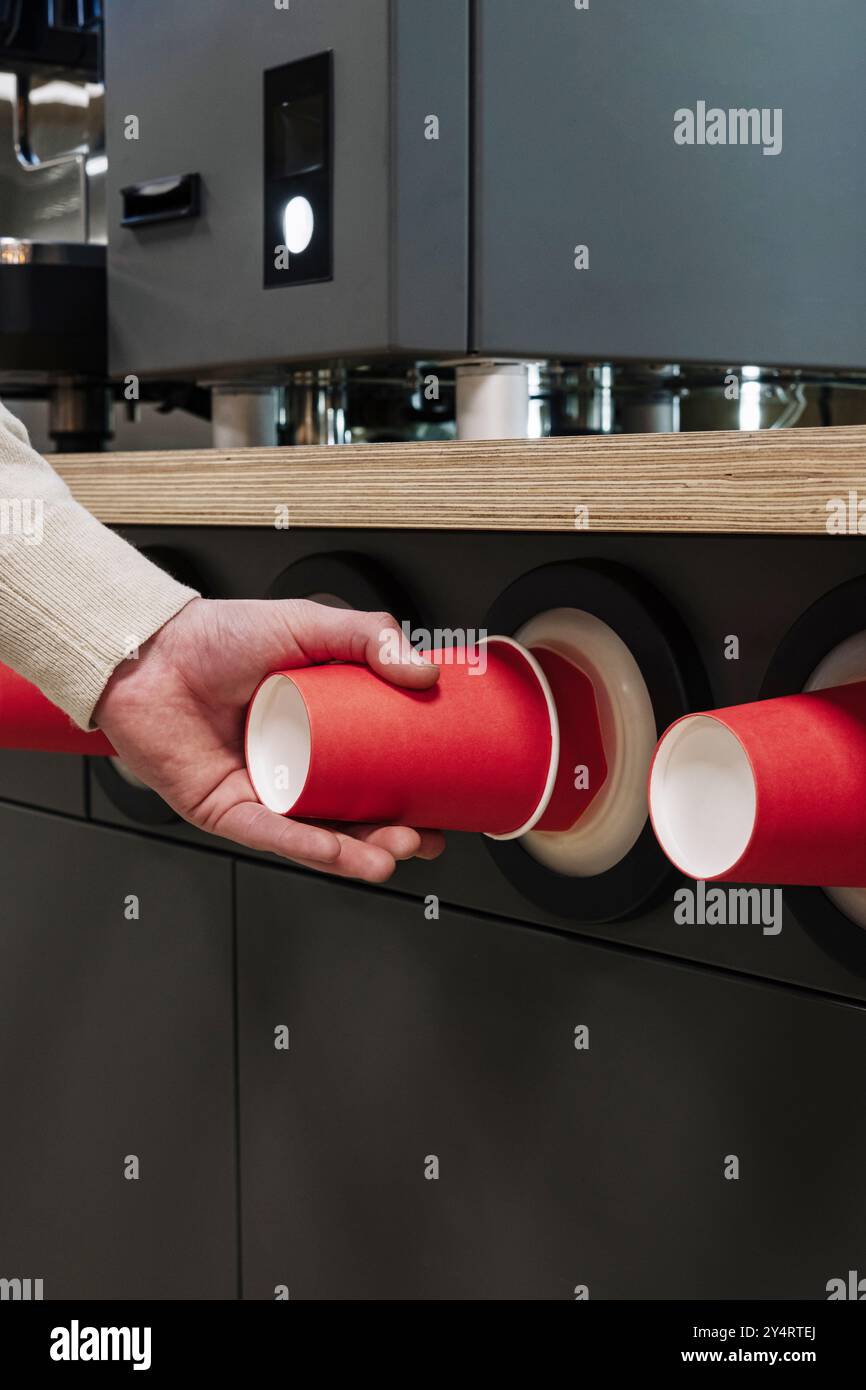 Close-up of a hand pulling a red paper cup from a modern cup dispenser ...