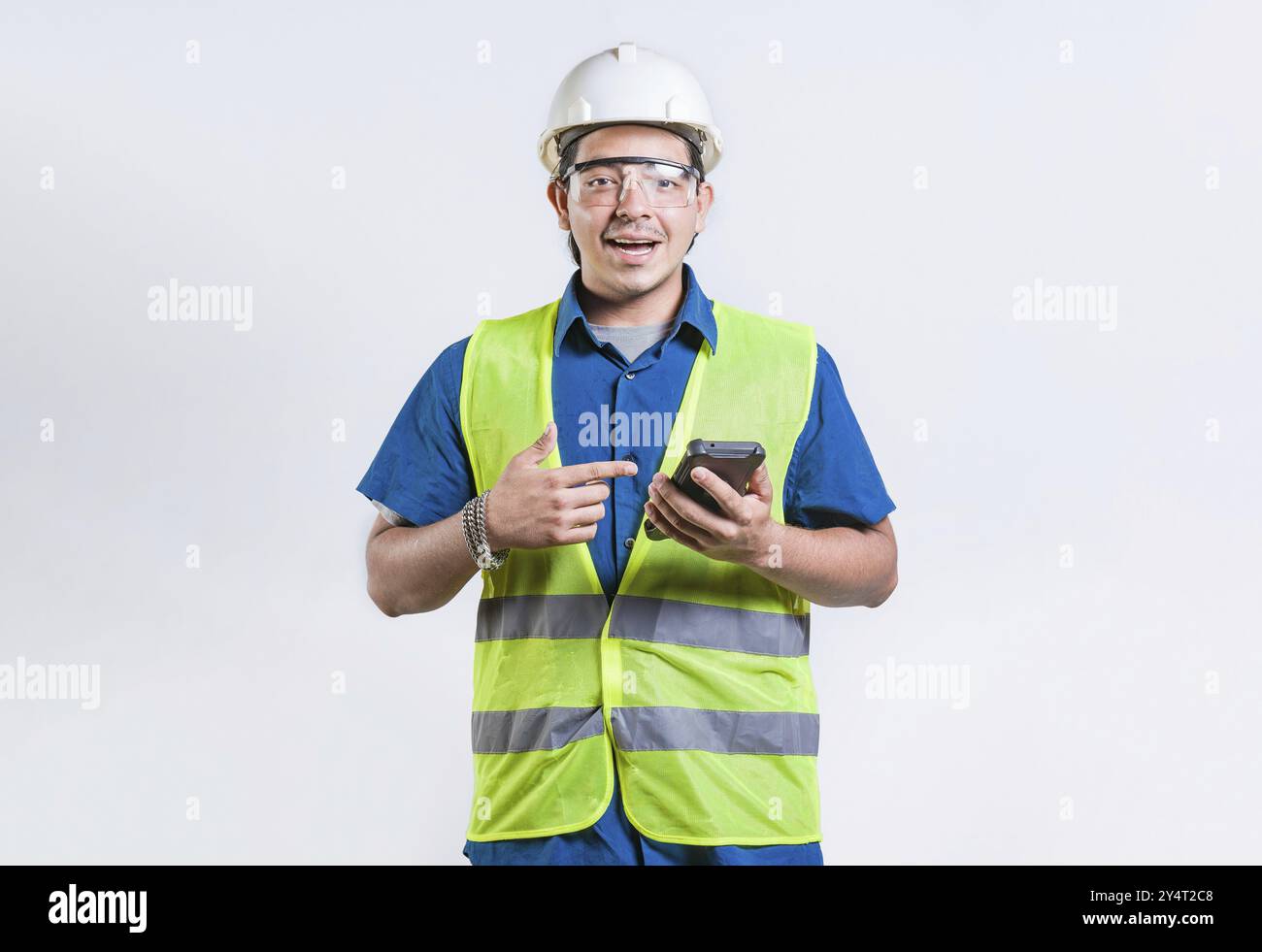Smiling engineer holding phone and looking at camera isolated. Latin male builder engineer using phone isolated Stock Photo