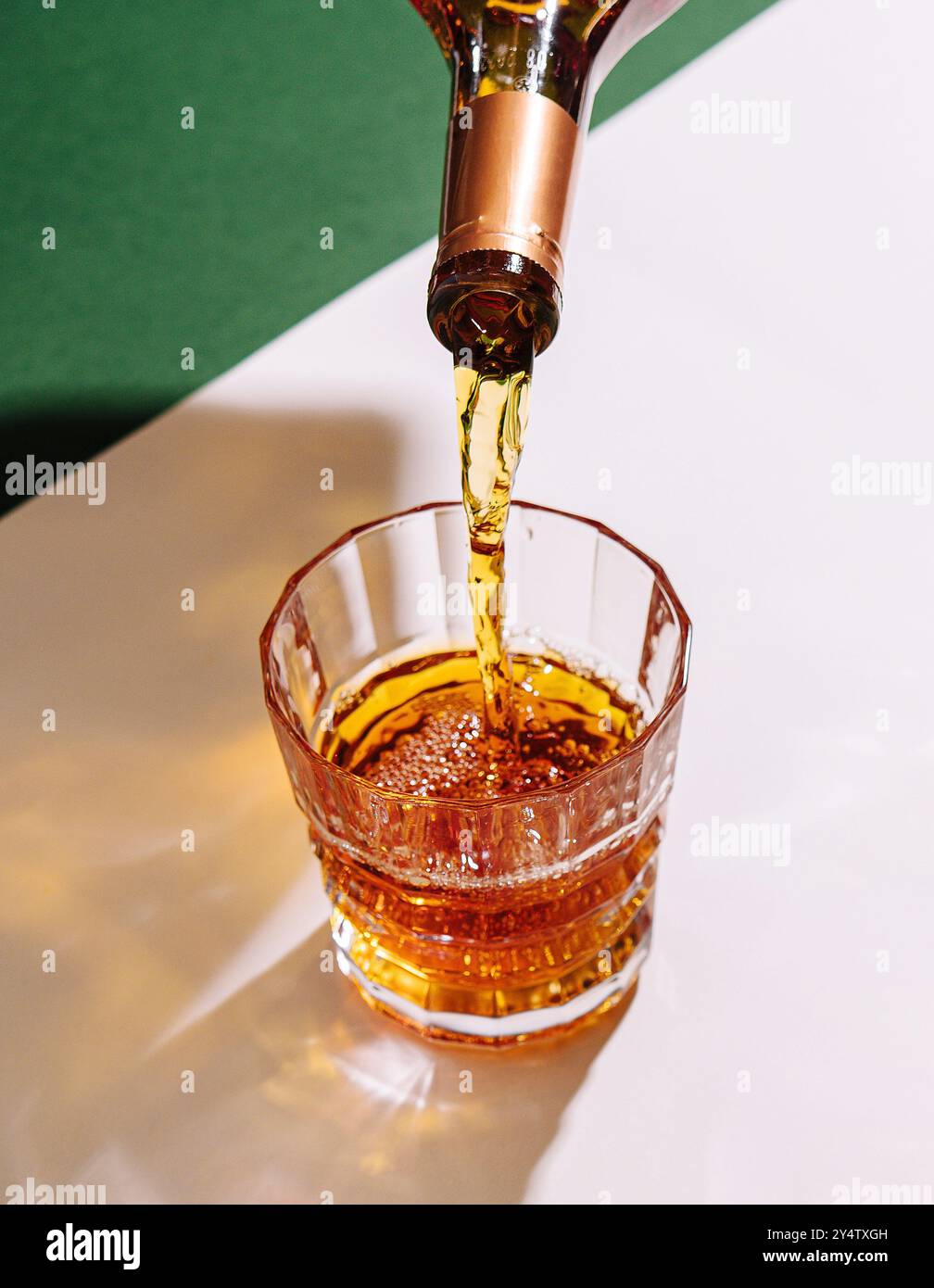 Bartender is pouring liquor from a bottle into a crystal tumbler, with two other tumblers on a table Stock Photo