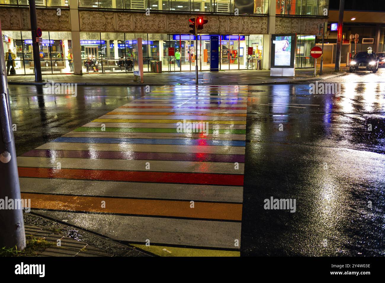 Rainy asphalt, zebra crossing in rainbow colours leads to the station, night shotLeoben, Styria, Austria, Europe Stock Photo