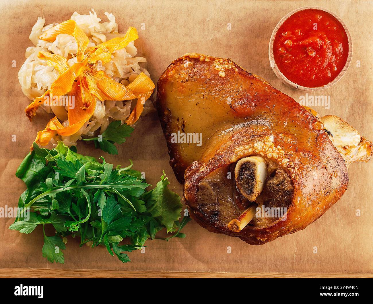 Delicious roasted pork knuckle served on wooden board with stewed cabbage, herbs and tomato sauce Stock Photo