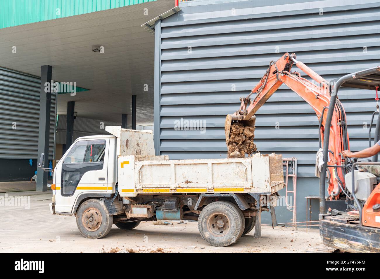 Small excavator loading soil onto dumper truck in construction site. Stock Photo