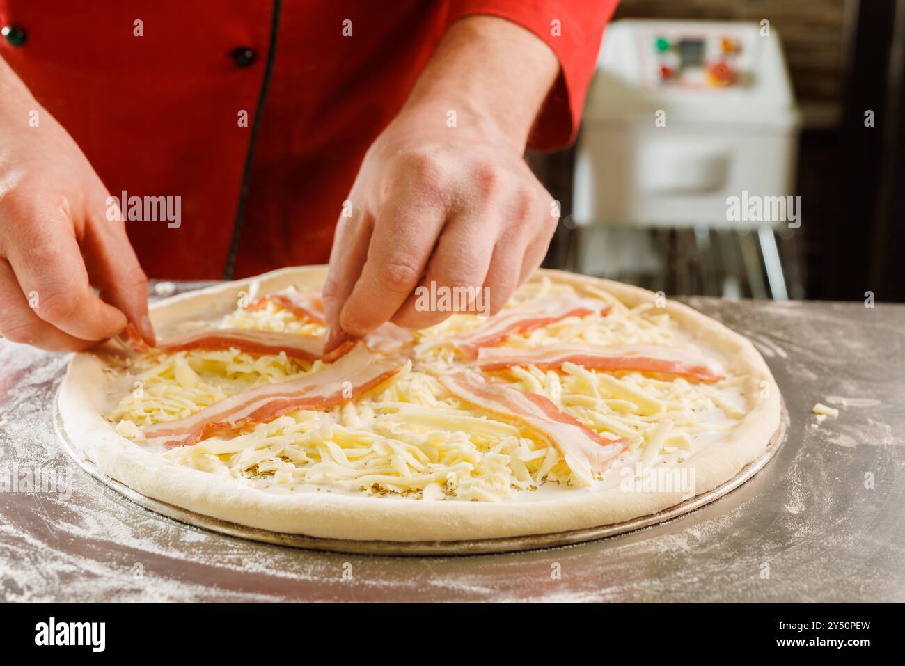 Close-up of a chef adding bacon to a cheese pizza before baking. Stock Photo