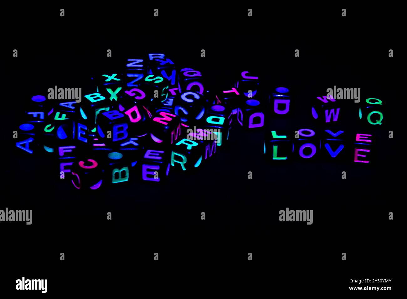 Neon-colored letters are scattered across a dark background with an emphasis on the word LOVE prominently displayed in the center Stock Photo