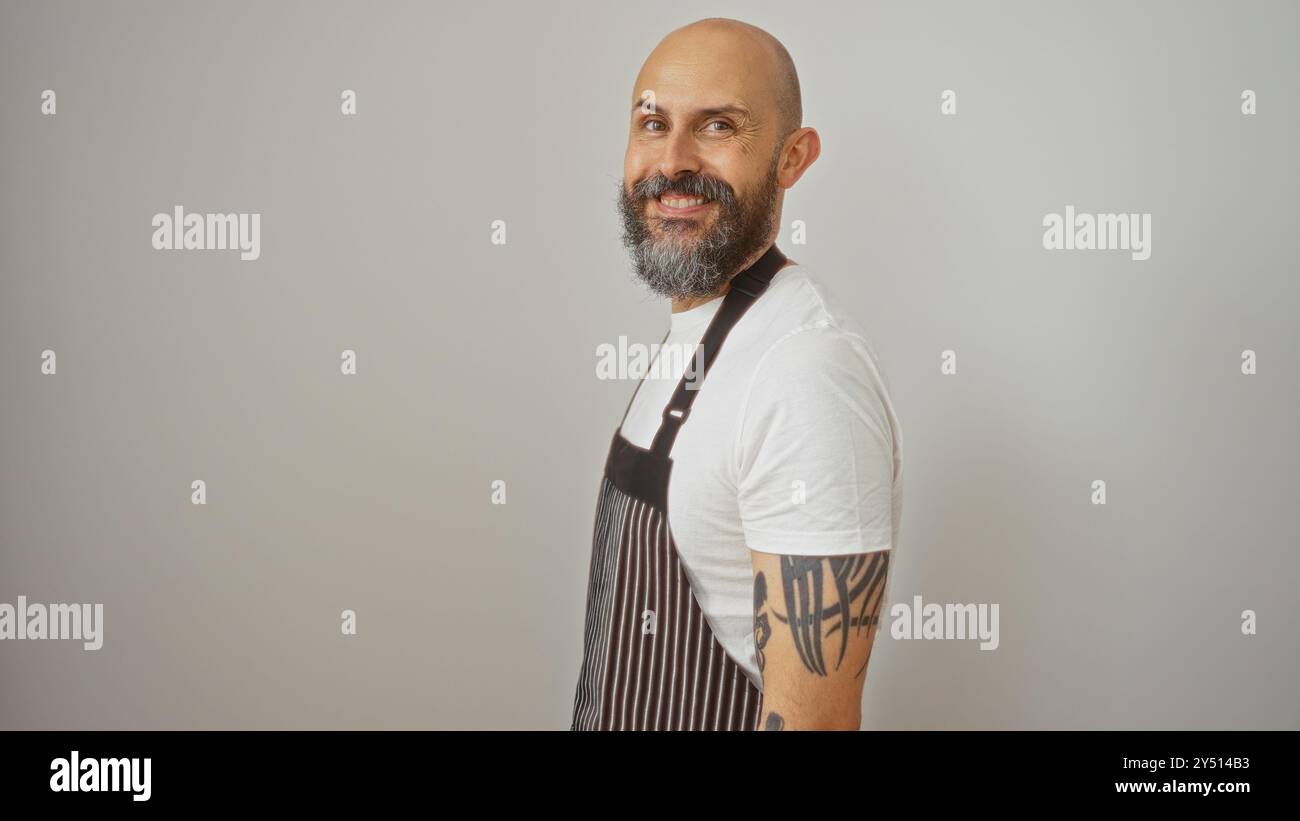 Hispanic man with a beard and tattoos, wearing an apron, smiling against a white background. Stock Photo