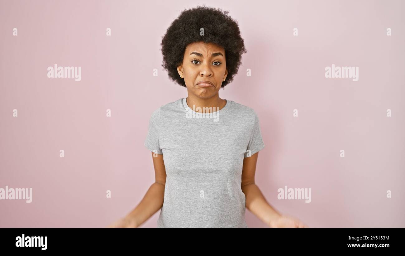 African american woman with curly hair standing against a pink isolated background, expressing confusion. Stock Photo