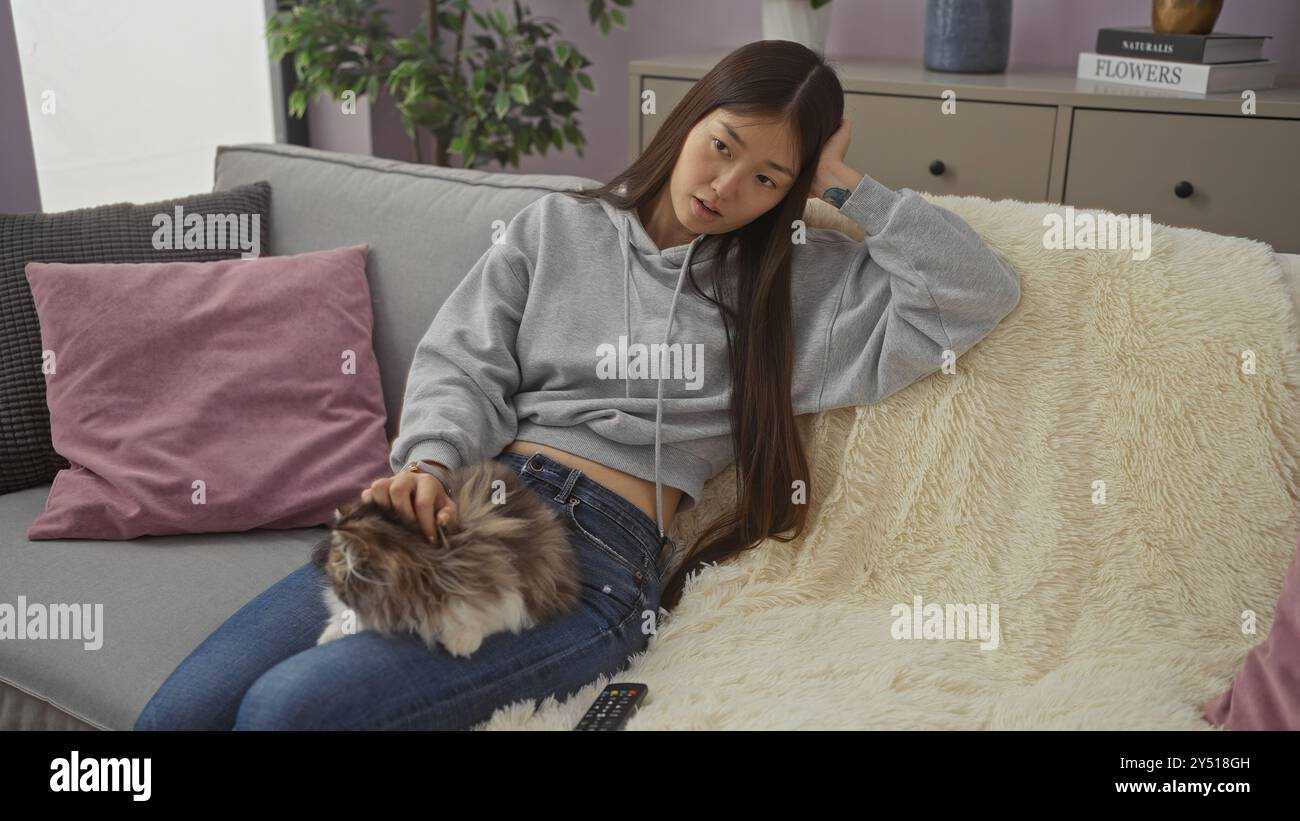 A young chinese woman lounges on a sofa with her cat in a cozy living ...