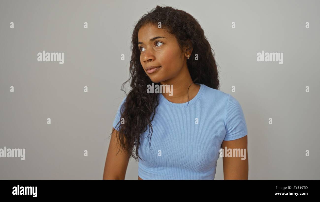Young woman with black curly hair wearing a blue shirt posing against a ...