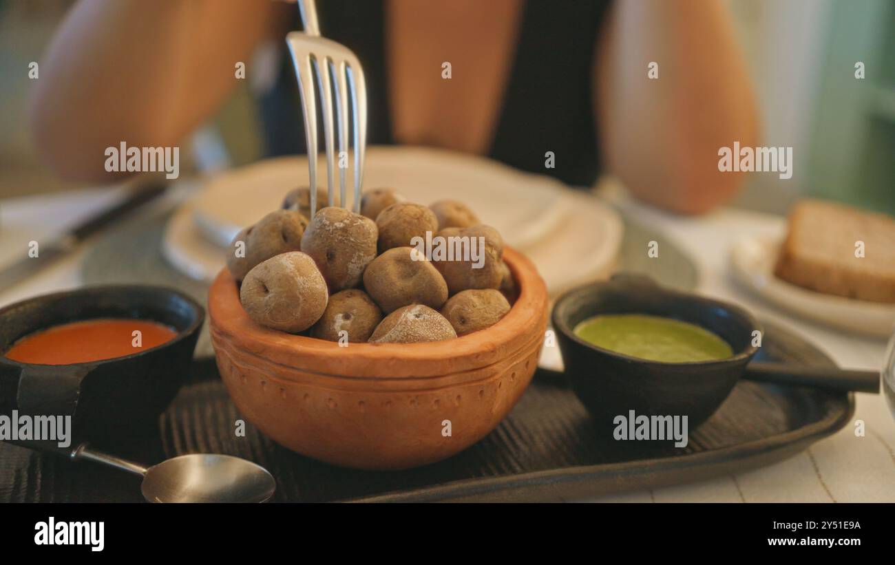 Woman enjoying papas arrugadas in a fancy indoor restaurant setting with dipping sauces and elegant tableware Stock Photo