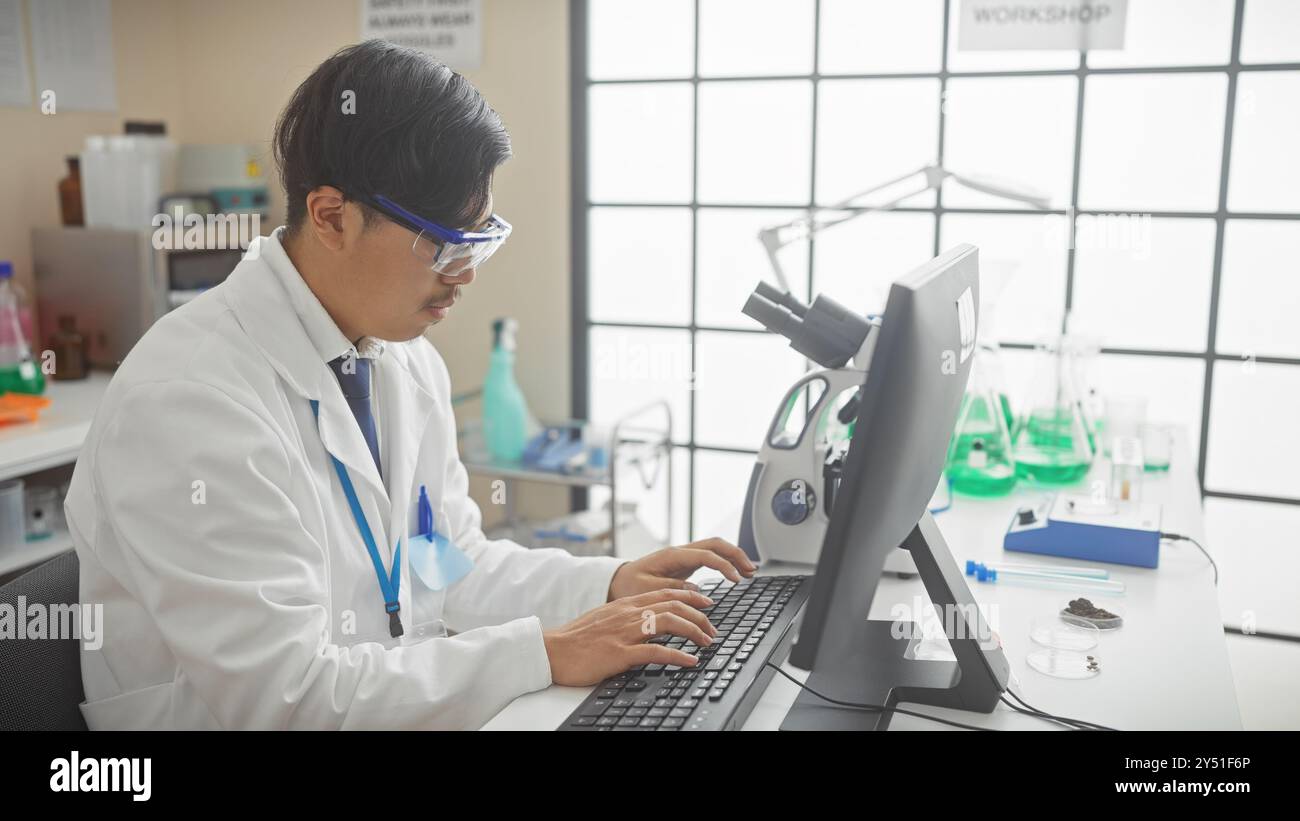 A young asian man in a lab coat working on a computer in a bright laboratory setting. Stock Photo